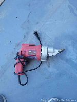 Photo of a red Northern Industrial branded electric shear with cord, metal blade housing, and trigger handle, placed on a flat grey surface.