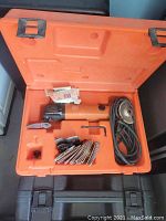 Orange electric Fein sander with power cord inside an open orange plastic carrying case along with a set of sanding discs in front.