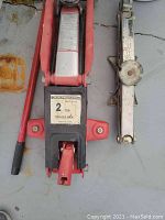 Two vehicle jacks: one red and black trolley jack labeled 2 ton, and one silver Honda scissor jack with a manual twist mechanism.