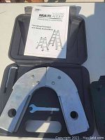 Photo of two metal ladder extender brackets, wrench tool, and instruction manual inside black plastic case.