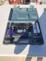 Central Pneumatic pneumatic nailer stored in a grey molded plastic hard case, showing the nailer with black metal and blue grip and additional accessories in the case compartments.