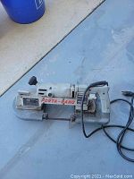 Full view of the Porta-Band two-speed portable band saw on a concrete floor, showing branding and power cord.