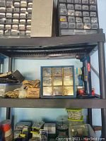 Middle black plastic shelf showing Ryobi cordless power drill on right, blue plastic organizer with hardware components, and multiple pairs of leather work gloves on left with smaller boxes of tools and hardware parts.
