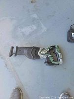 Top-down image of the Hitachi CR 18DL reciprocating saw laid flat on a concrete surface, showing the entire saw body with black and camo green handle and no blade attached.