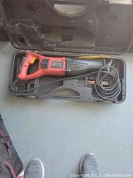 Red and black Sears Roebuck reciprocating saw in black plastic carrying case on a flat surface, with power cord coiled.