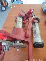Photo of Hornady red cast metal reloading press with attached clear powder measure and mechanical handle, placed on wooden surface.