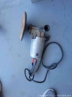 Electric heavy-duty sander with round sanding pad and power cord placed on concrete floor.