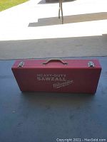 Closed red metal carrying case with handle, labeled 'Heavy-Duty Sawzall Milwaukee'