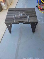 Portable tool stand with ribbed top surface and cut-outs for mounting, foldable black metal legs shown on concrete floor