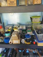 Shelf with various wire spools, tape rolls, boxes, and plastic bins containing screws and fasteners.