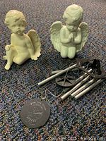 Two garden angel figurines with a small windchime laid on the floor