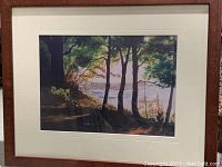 Framed watercolor landscape print showing trees near water with matting and wood frame.