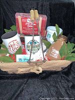 Full basket containing hot cocoa themed gift items arranged with greenery inside a woven basket.
