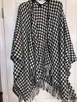 Full view of black and white houndstooth shawl wrap hanging on hanger, showing fringed edges.