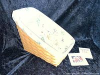 Photo showing Longaberger woven catalog basket with floral fabric liner inside, placed on black background with informational cards beside it.