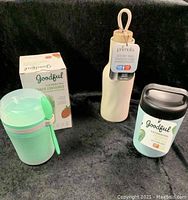 Photo showing the trio of containers including the Goodful snack container with its box, the Goodful food jar, and the Primula insulated water bottle with a white body and wood top.