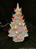 Front view of the ceramic Christmas tree lit up with colorful bulbs on a black background.