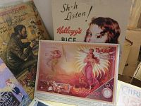 Photo showing several reproduction tin advertising signs including Kellogg's Rice and Frank Leslie's Almanac with vintage artistic graphics.