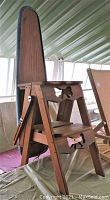 Side view of antique wooden 3-in-1 step ladder showing foldable design and ironing board pad covered with quilted cloth.