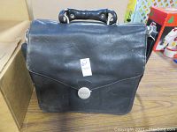 Closed black leather Dell laptop bag showing flap and metal logo clasp with some light scratches.
