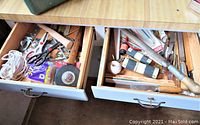 Two open wooden tool bench drawers showing various hand tools and accessories within.