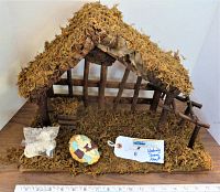 Wooden nativity manger with moss, ceramic baby Jesus figure on the floor and sealed bag of ceramic pieces.