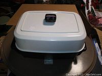 Rectangular electric skillet with white lid and black temperature control knob on top.
