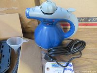 Blue Scunci Pro Steam portable steamer with power cord coiled beside it, placed on cardboard.