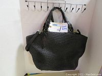 Black woven texture handbag with two short handles and a long adjustable shoulder strap hanging on hooks