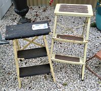 Both vintage 3-step ladders, one metal Ekco with black steps and one wooden with black steps, positioned upright outdoors on gravel surface.