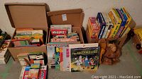 Boxes with vintage children's books upright, several colorful covers visible, along with a child's plush Muppet-like toy and stacked boxed games.