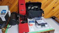 Overhead view of all items including telephoto lens in case, Metz flash unit, flash frame, JBL speaker box, and black carrying case.