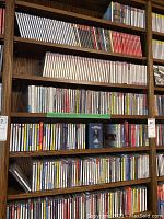 Wooden shelves filled with rows of CD jewel cases showing multiple labels and uniform arrangement.