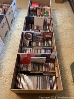 Four cardboard storage boxes on carpet, each packed with rows of CD jewel cases