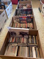Five cardboard boxes filled with rows of audio CDs in jewel cases, arranged on floor