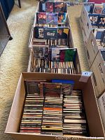 Overhead view of four cardboard boxes filled with assorted music CDs on carpeted floor