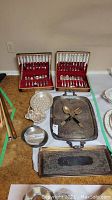 Overview of two flatware boxes, trays, bowl and serving utensils on floor
