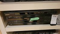 Front view of Sony DVD player stacked above Pioneer LaserDisc player on a white shelf with price tag visible.