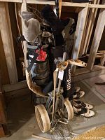Multiple golf clubs in a golf bag displayed with a wheeled golf cart and shoes.