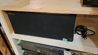 Front view of Mirage MC-si speaker with black grille cloth and power cord coiled beside.
