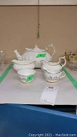 Photo showing full set including teapot, creamers, and sugar bowls arranged on a table with green tape marking area.
