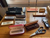 Overall view of vintage collectible pens including Sheaffer, Parker, and Cross with original cases and pen holders on a wooden desk.