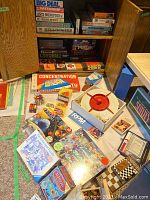 Various vintage board games stacked on shelves and spread on the carpet, showing numerous game boxes and some opened games, including Rubik's cubes and puzzles.