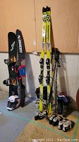 Overall view of the skis, snowboards, boots, helmet, and goggles leaning against wall in basement