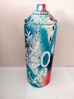 Front view of the painted spray can showing white graphic motifs and vibrant splattered paint.