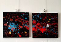 Front view of two square abstract paintings mounted on wall, showing vibrant splatters and textured layers