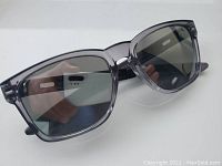 Oakley Catalyst sunglasses, front view showing transparent gray frame and chrome lenses, held at an angle.