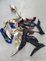 Multiple pairs of women's shoes stacked against a plain white background, featuring various styles, colors, and heel types.