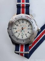 Front view of the watch showing white dial, compass bezel, and striped nylon strap.