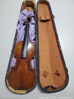 Full violin in open violin case showing front side of instrument with fingerboard and scroll, no strings or bridge, case worn inside.